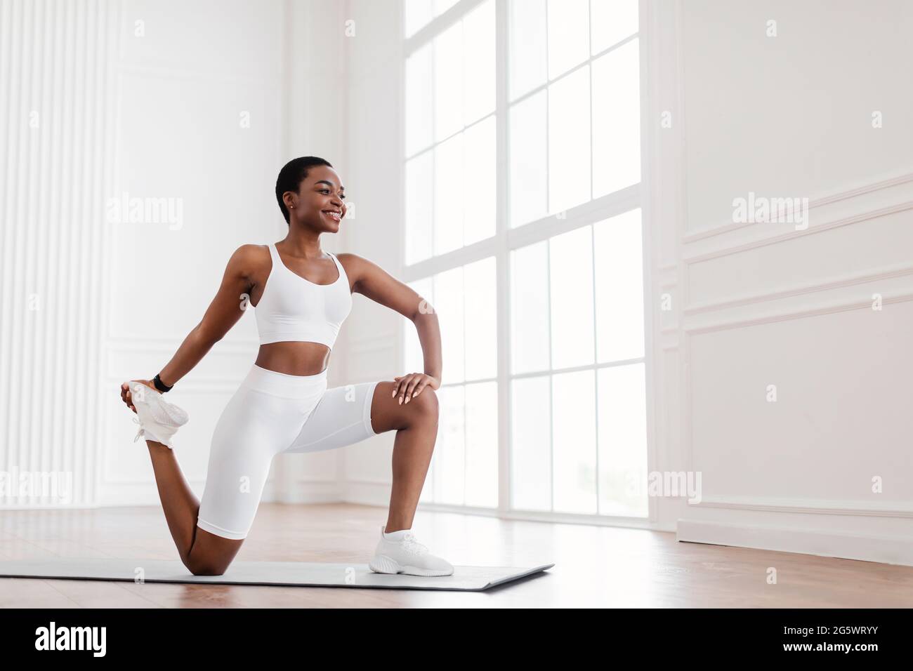 Junge schwarze Frau dehnt das Bein auf einer Yogamatte Stockfoto