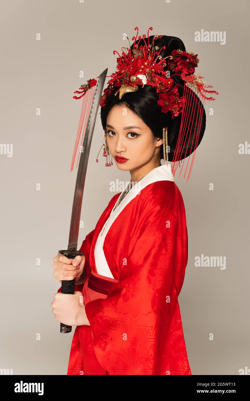 Asiatische Frau in Nationalkostüm hält Schwert isoliert auf grau Stockfoto