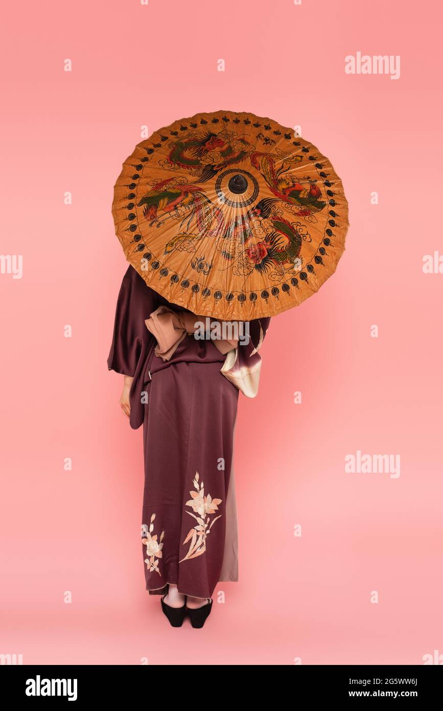 Rückansicht einer asiatischen Frau mit traditionellem Regenschirm auf rosa Hintergrund Stockfoto