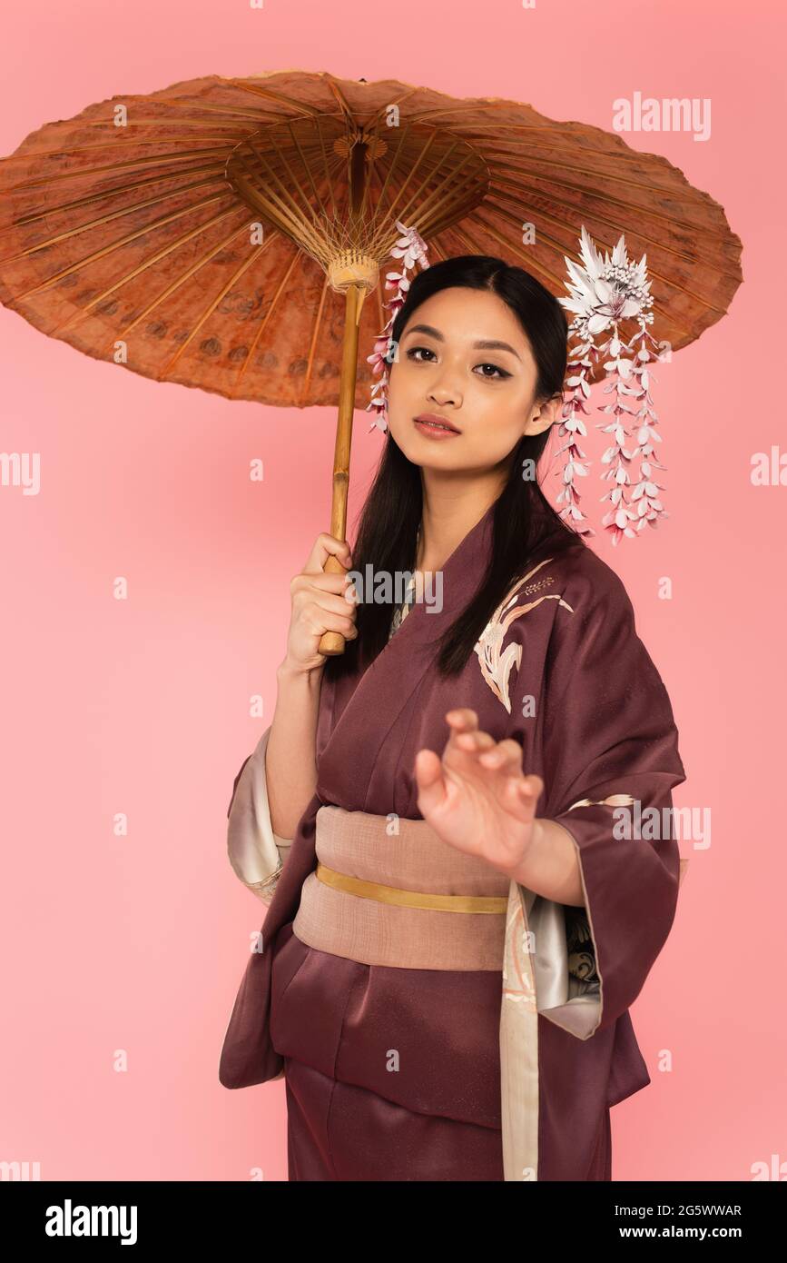 Hübsche japanische Frau mit Regenschirm posiert isoliert auf rosa Stockfoto