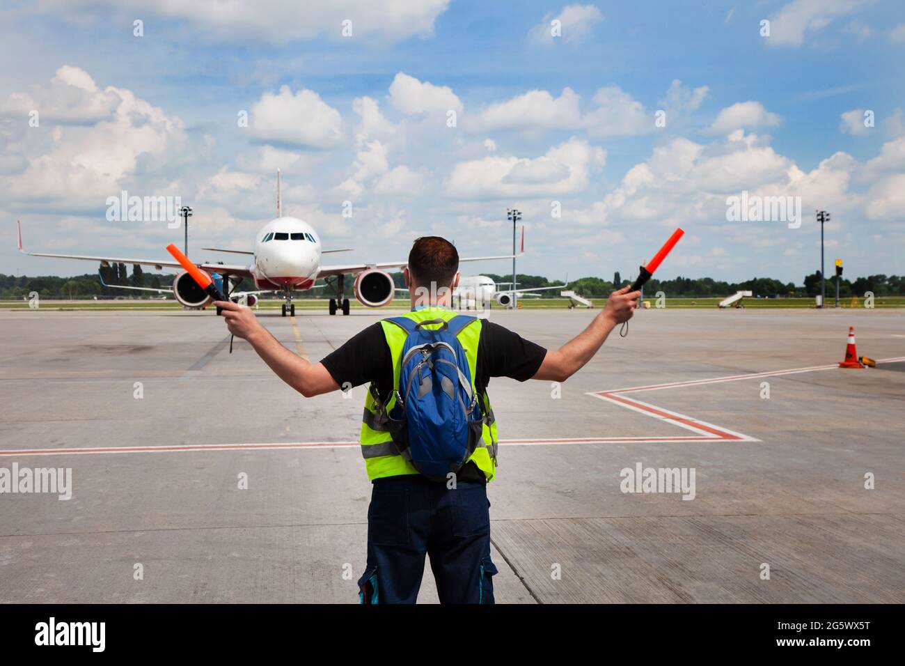 Der Verkehrskontrolleur am Flughafen zeigt die Semaphore mit Stöcken zum Piloten des Flugzeugs, wo er parken soll. Ankunft des Flugzeugs auf der Landebahn. Handling-Service Stockfoto