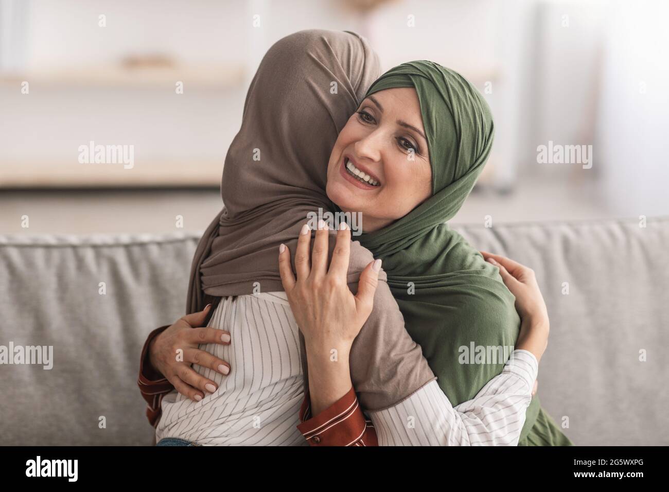 Ältere Muslimische Mutter Und Erwachsene Tochter In Hijab, Die Sich Im Indoors Umarmt Stockfoto