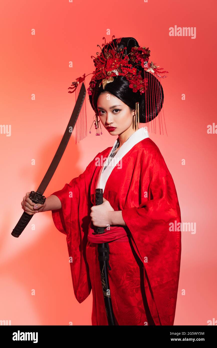 Japanische Frau in authentischem Kostüm mit Scheide und Schwert auf rotem Hintergrund Stockfoto
