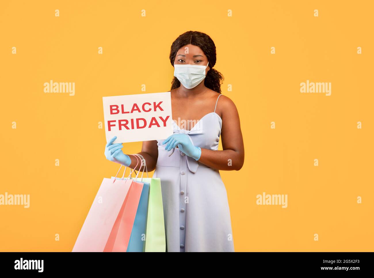 Schwarze Frau trägt Gesichtsmaske, hält SCHWARZES FREITAGSSCHILD, hält Einkaufstaschen, kauft während des Coronavirus Dinge Stockfoto