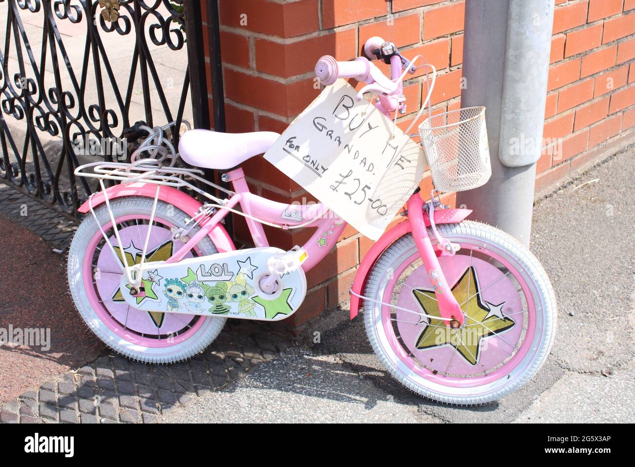 Kinder rosa Fahrrad mit Verkauf Schild mit der Aufschrift "Buy Me Granddad for only £25.00". Cleveres Werbekonzept Stockfoto