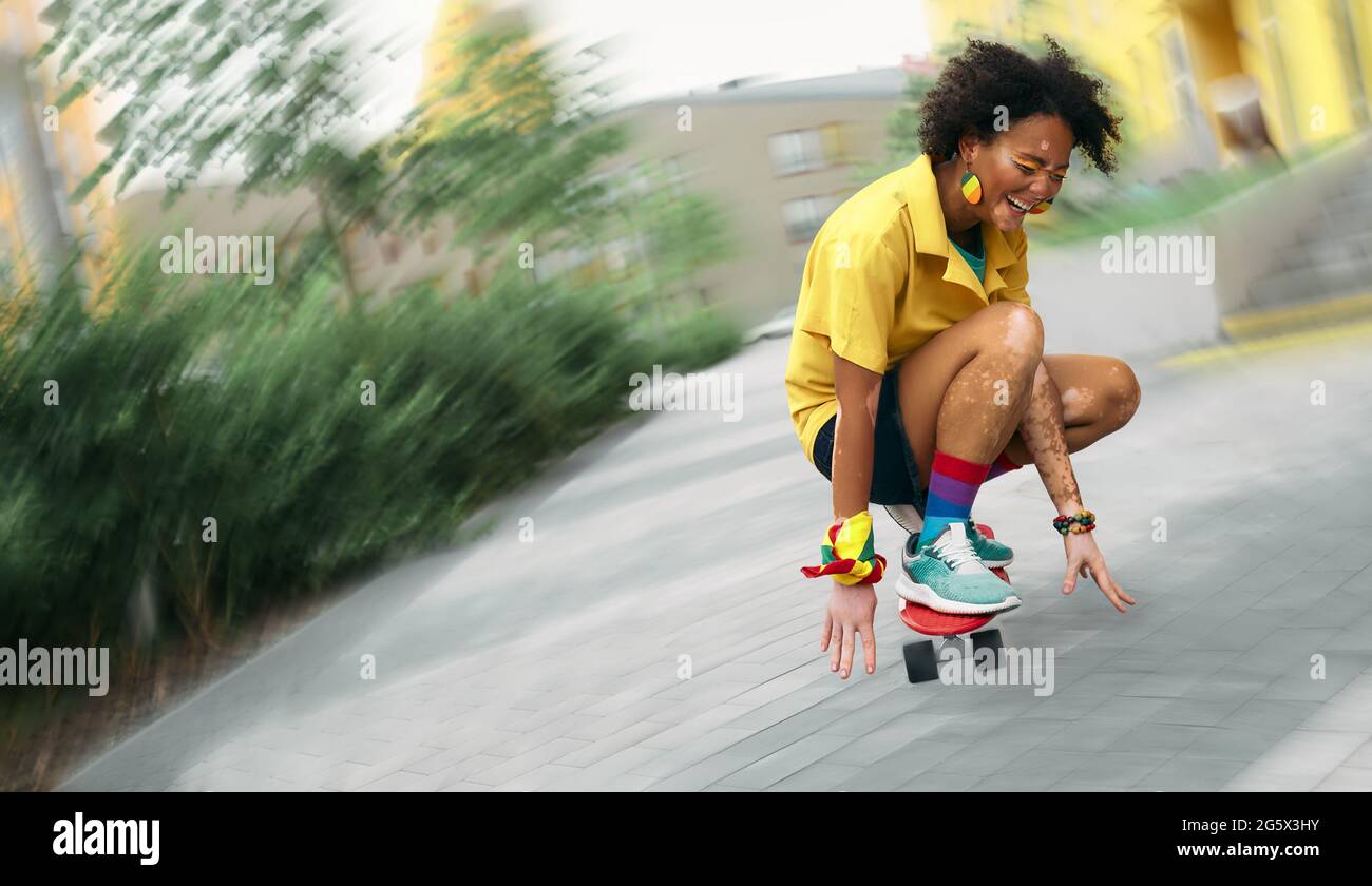 Afroamerikanische Frau mit Vitiligo begeistert mit Skateboarding auf der modernen Stadtstraße. Unscharfer Fokus Stockfoto