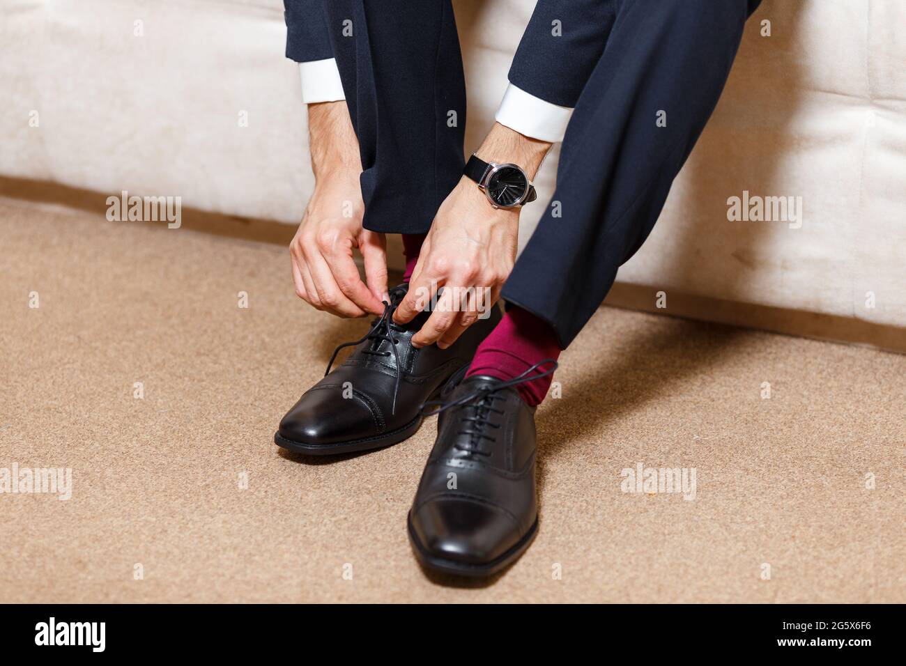 Ein Geschäftsmann in dunkelblauem Anzug, roten Socken und Uhren, der seine  Schnürsenkel mit schwarzen Schuhen bindet. Moderner, stilvoller und teurer  Look für junge Männer Stockfotografie - Alamy