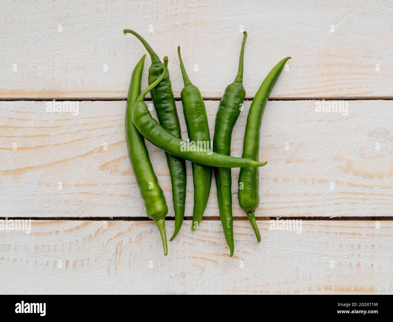 Grundansicht von grünen Chilischoten auf einem weißen, rustikalen Hintergrund mit Holztäfelung. Stockfoto