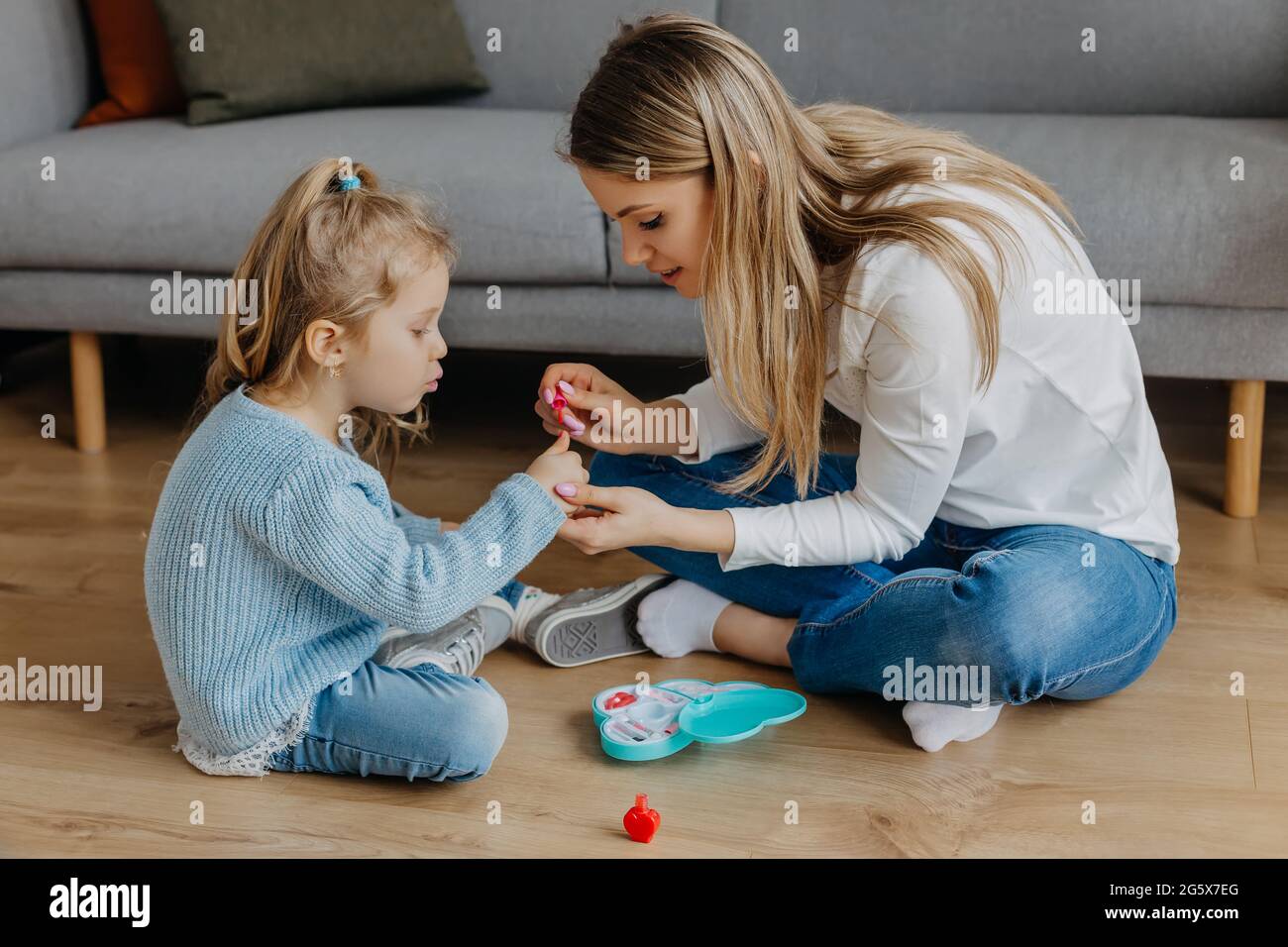 Mutter und kleine Tochter malen ihre Nägel mit Spielzeug-Nagellack. Kind spielt mit Mutter zu Hause. Konzept der guten Elternschaft und glückliche Kindheit, Familie Stockfoto