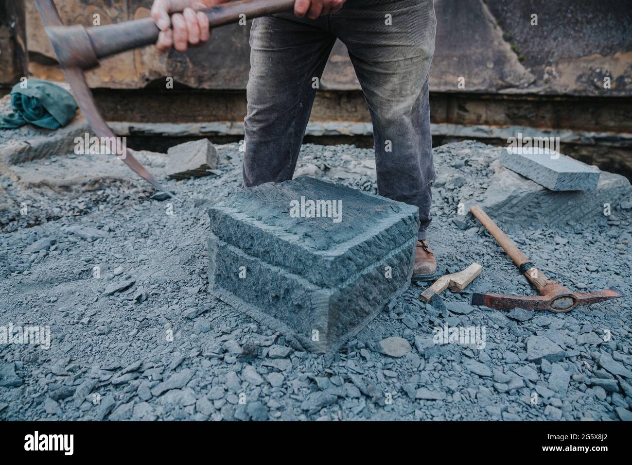 Handwerker, der einen quadratischen Block aus Cancagua-Stein mit einem Steinpflücken formt, am Ufer der Stadt Ancud, Chiloe Island. Stockfoto