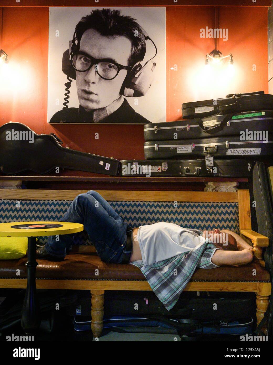 Bandmitglied von Los Pacaminos schläft nach einem Live-Konzert im Londoner Half Moon Putney Pub unter dem Bild von Elvis Costello. Stockfoto