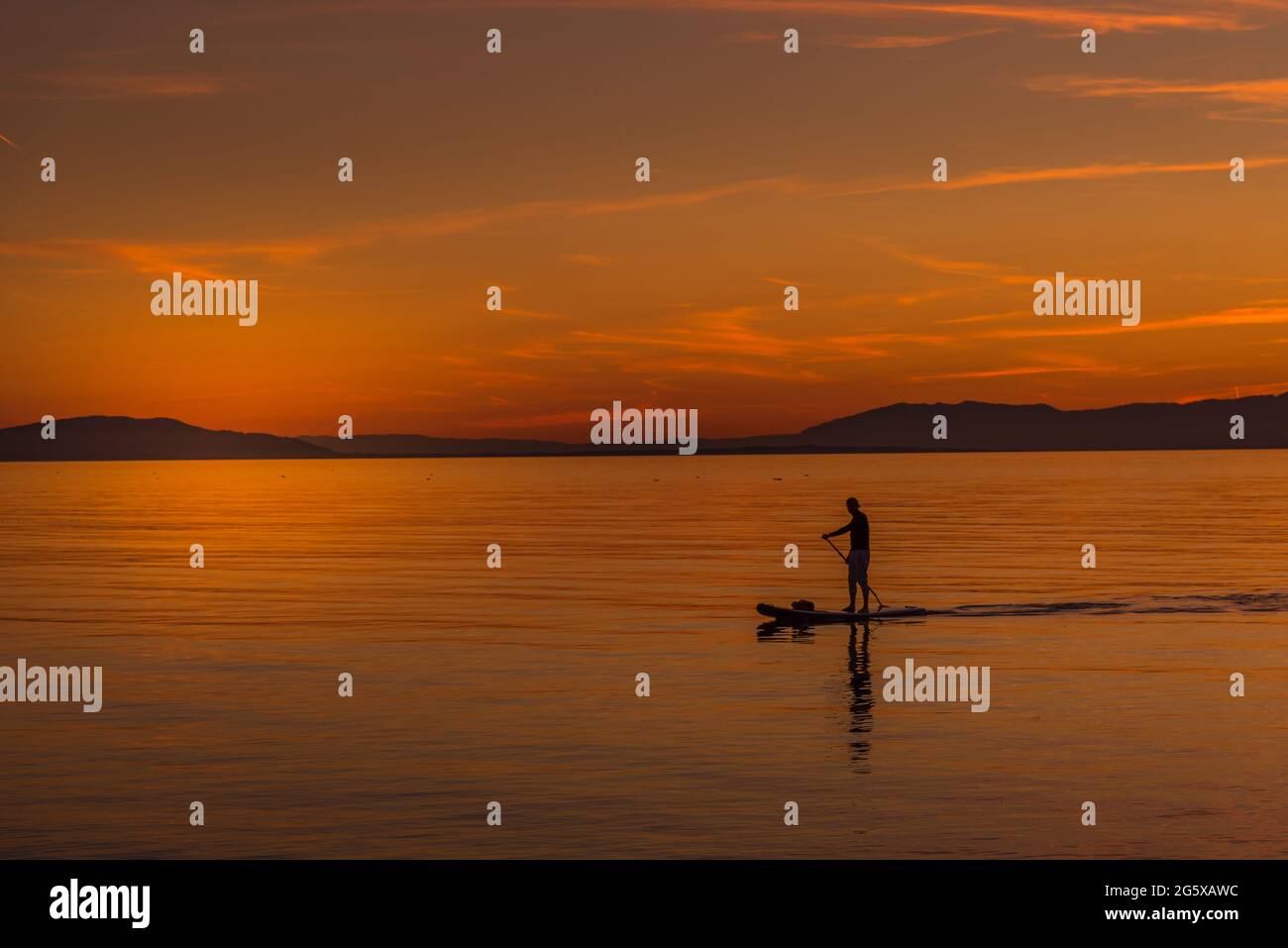 Unerkannte Person, die den Sonnenuntergang an der Küste von einem Body-Board-Tisch aus genießt. Stockfoto