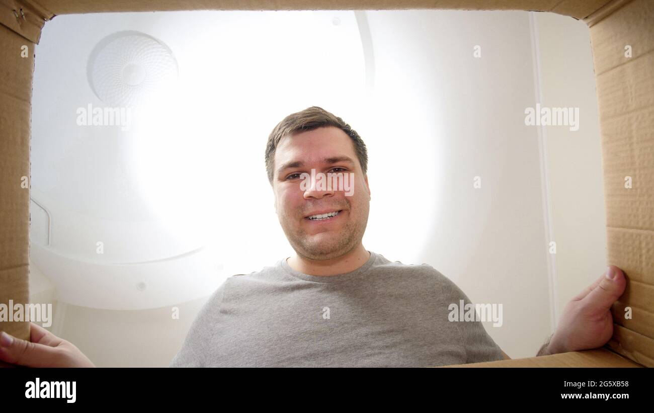Junger lächelnder Mann, der in das Paket oder den Geschenkkarton schaut Stockfoto