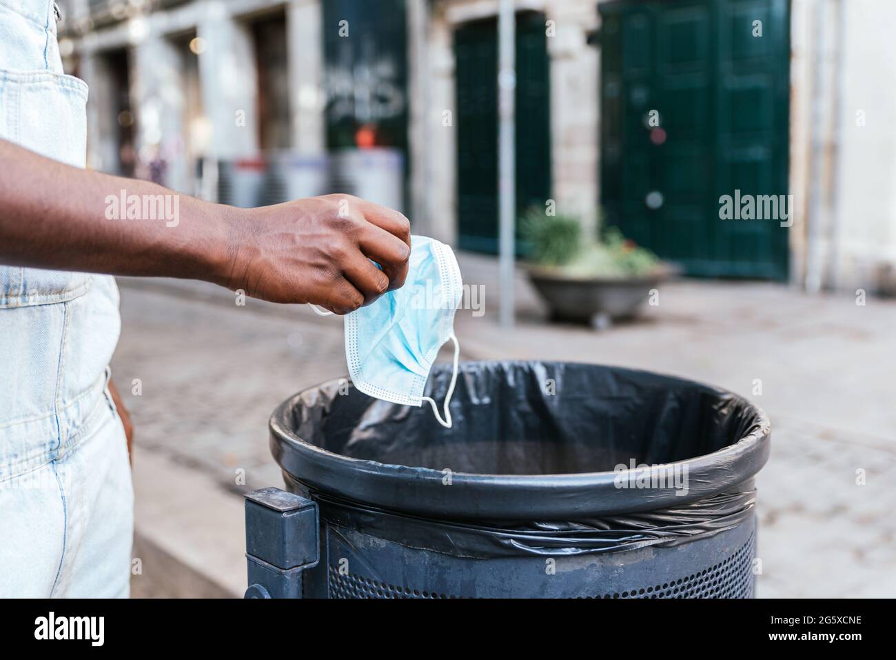 Hände eines unerkennbaren jungen schwarzen Mannes, der eine Gesichtsmaske in einen Papierbehälter wirft. Konzept des Endes der Covid19-Pandemie Stockfoto