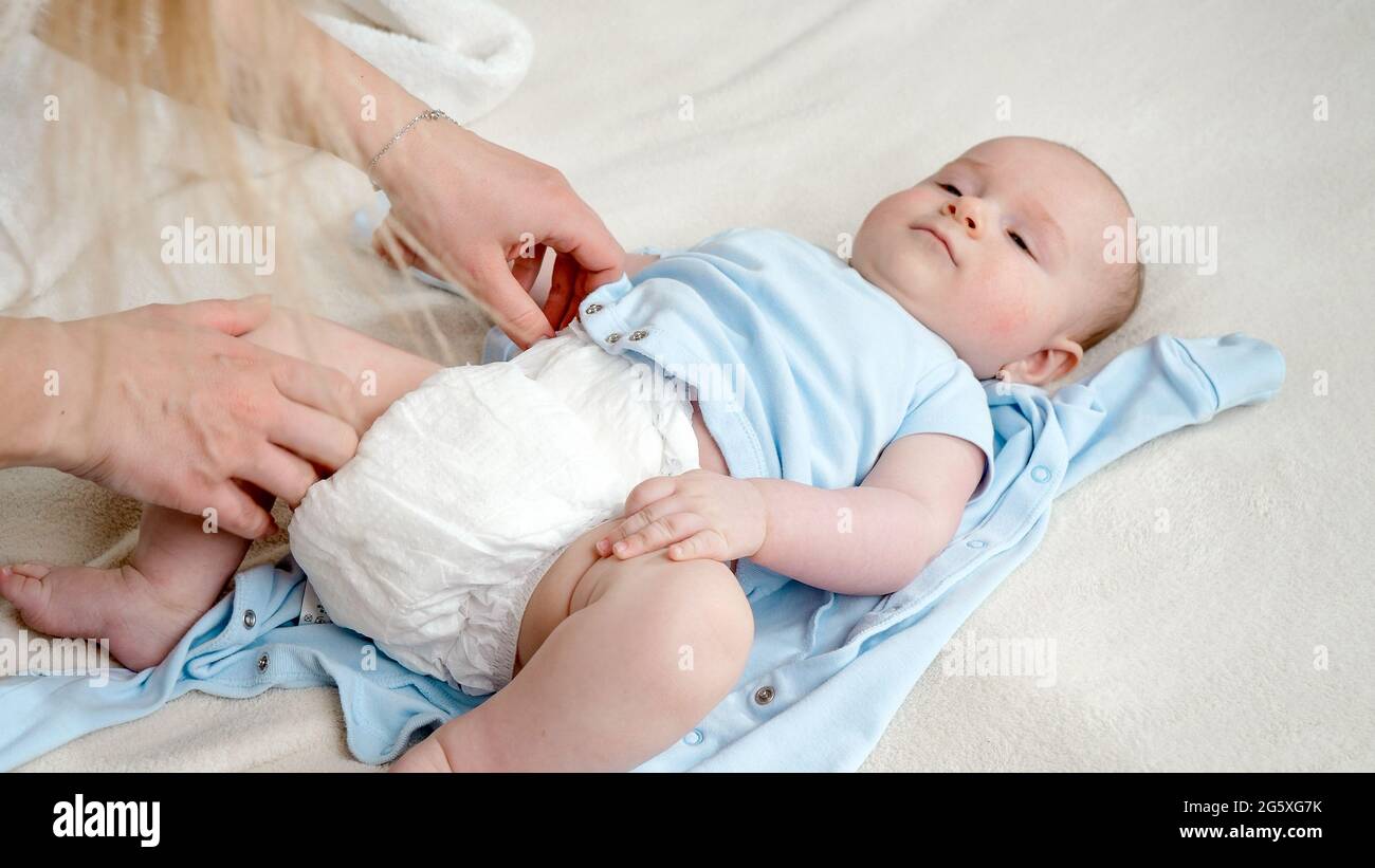 Nahaufnahme der Mutter, die unordentliche Windeln zu einem kleinen, im Bett liegenden Sohn gewechselt hat Stockfoto