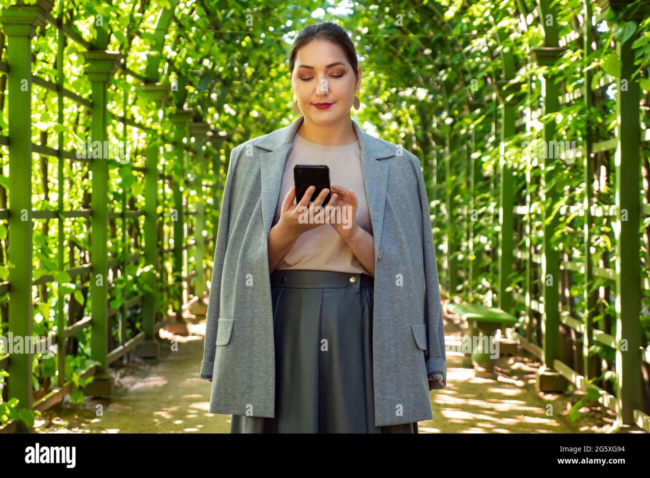 Junge Geschäftsfrau mit Telefon unter einem lebenden Bogen im Park Stockfoto