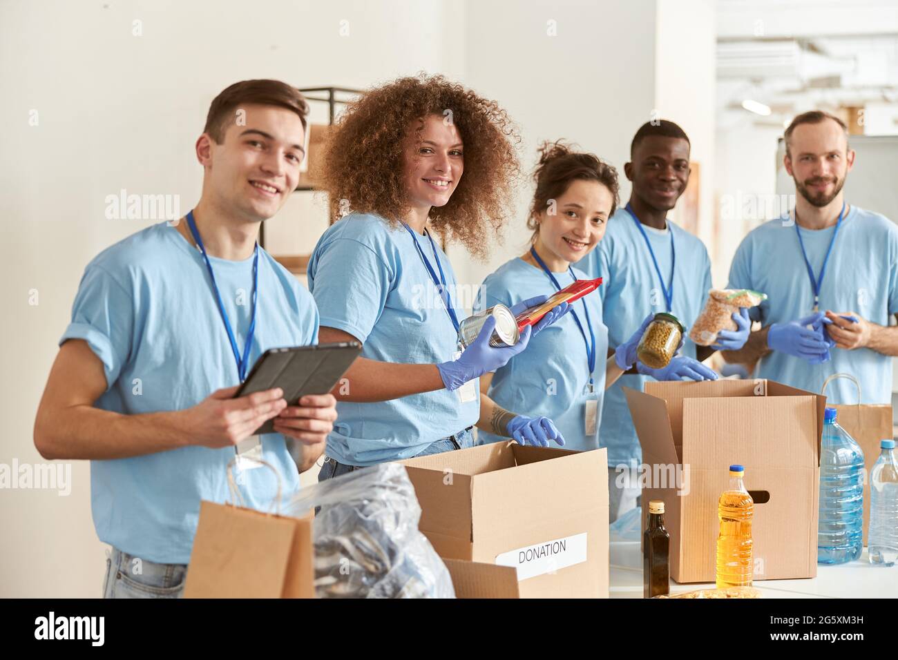 Porträt glücklicher Freiwilliger, die die Kamera anlächeln, während sie sortieren, Lebensmittel in Kartons packen und gemeinsam an einem Spendenprojekt in Innenräumen arbeiten Stockfoto