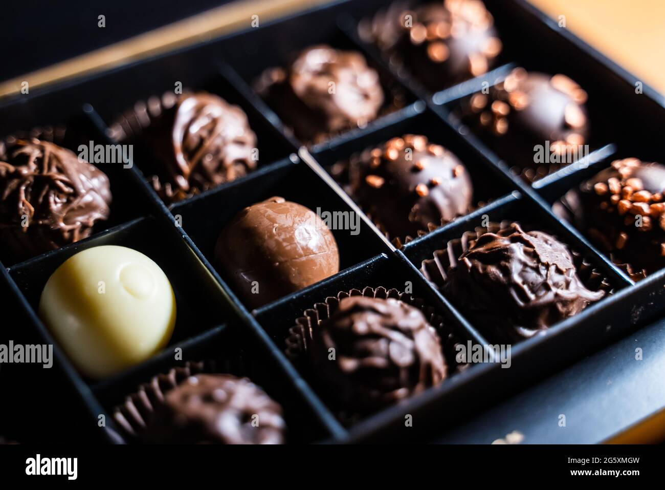 Mehrere Sorten von Schokoladentrüffeln mit schokoladiger und milchiger Glasur und goldenen Streuseln mit Nüssen. Runde Trüffelkugel in einer quadratischen Schachtel schneiden. Stockfoto