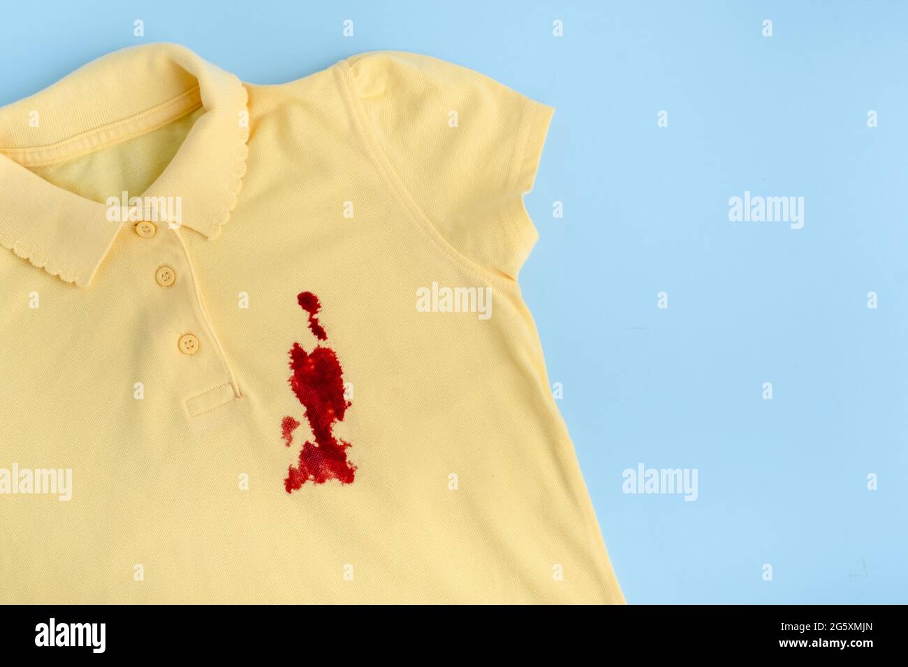 Blutflecken auf einem gelben T-Shirt. Platz für Text. Isoliert auf blauem Hintergrund. Hochwertige Fotos Stockfoto