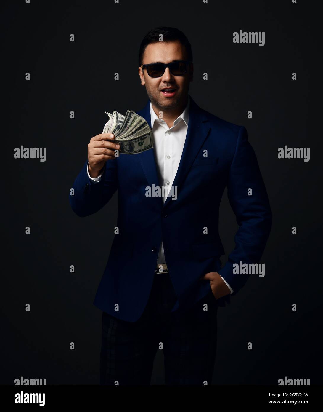 Porträt eines unverschämten Brunet-Geschäftsmannes in blauer Jacke und Sonnenbrille, der mit Geldfan in der Hand steht Stockfoto