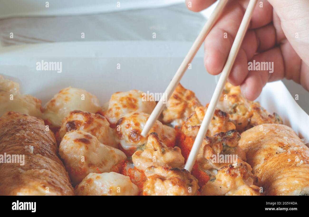 Hand halten Rolle mit Essstäbchen Nahaufnahme. Lunchboxen, Sushi-Set. Verschiedene Rollen auf hellem Hintergrund. Lieferung im Restaurant, Konzept zum Mitnehmen. Japan Stockfoto