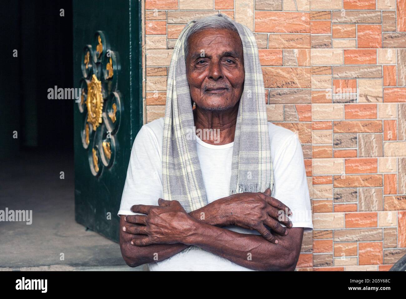 Älterer indischer Mann mit grauem Haar, grauem Schal über Kopf und Armen gefaltet Posen vor seinem Haus, Trichy, Tamil Nadu, Indien Stockfoto