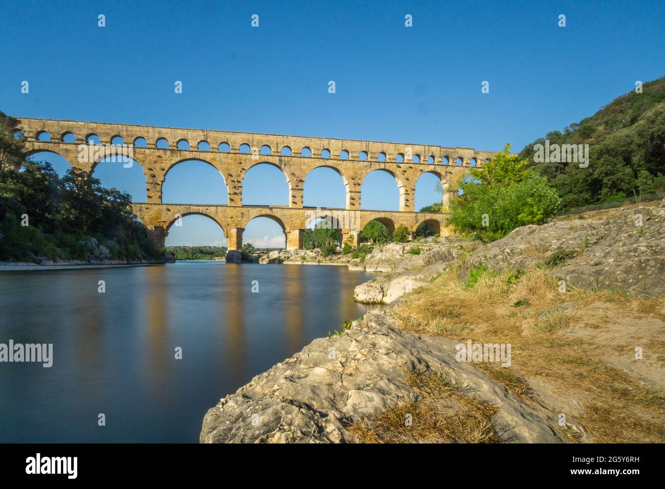 Römisches Aquadukt Pont du Gard zur goldenen Stunde mit ruhigem Fluss in der Nähe von Avignon, Frankreich Stockfoto