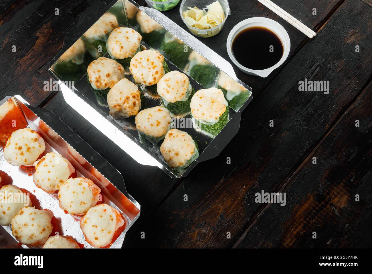 Sushi-Brötchen zum Mitnehmen in Behältern, philadelphia-Brötchen und gebackene Garnelenrollen auf altem dunklen Holztisch im Hintergrund, mit Platz für Kopieplatz und Platz Stockfoto