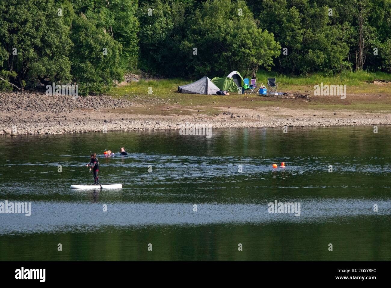 Loch Venachar, Loch. Lomonnd und Trossachs National Park, Schottland, Großbritannien. 30. Juni 2021. IM BILD: Zelte auf der loch-Seite und Leute auf dem Wasser paddeln, Kajakfahren, wild schwimmen und genießen das heiße Sommerwetter während einer Zeit, in der die schottischen Seen leer sind. Der große steinerne Strand liegt um den loch herum, der normalerweise komplett unter Wasser wäre, aber bei dem langen trockenen und heißen Wetter gibt es nichts, was das verdunstende Wasser ersetzen könnte. Quelle: Colin Fisher/Alamy Live News Stockfoto