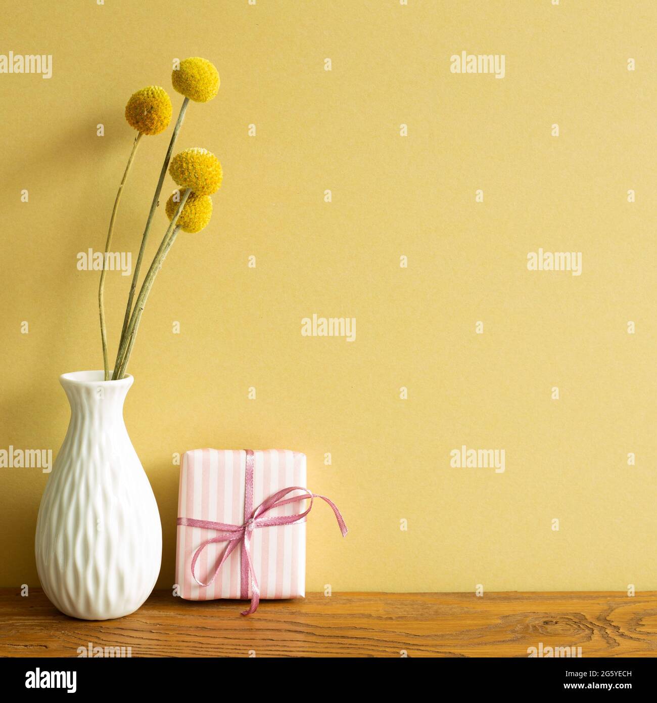 Rosa Geschenkbox, Vase mit trockenen Blumen auf Holztisch. Gelber Wandhintergrund Stockfoto
