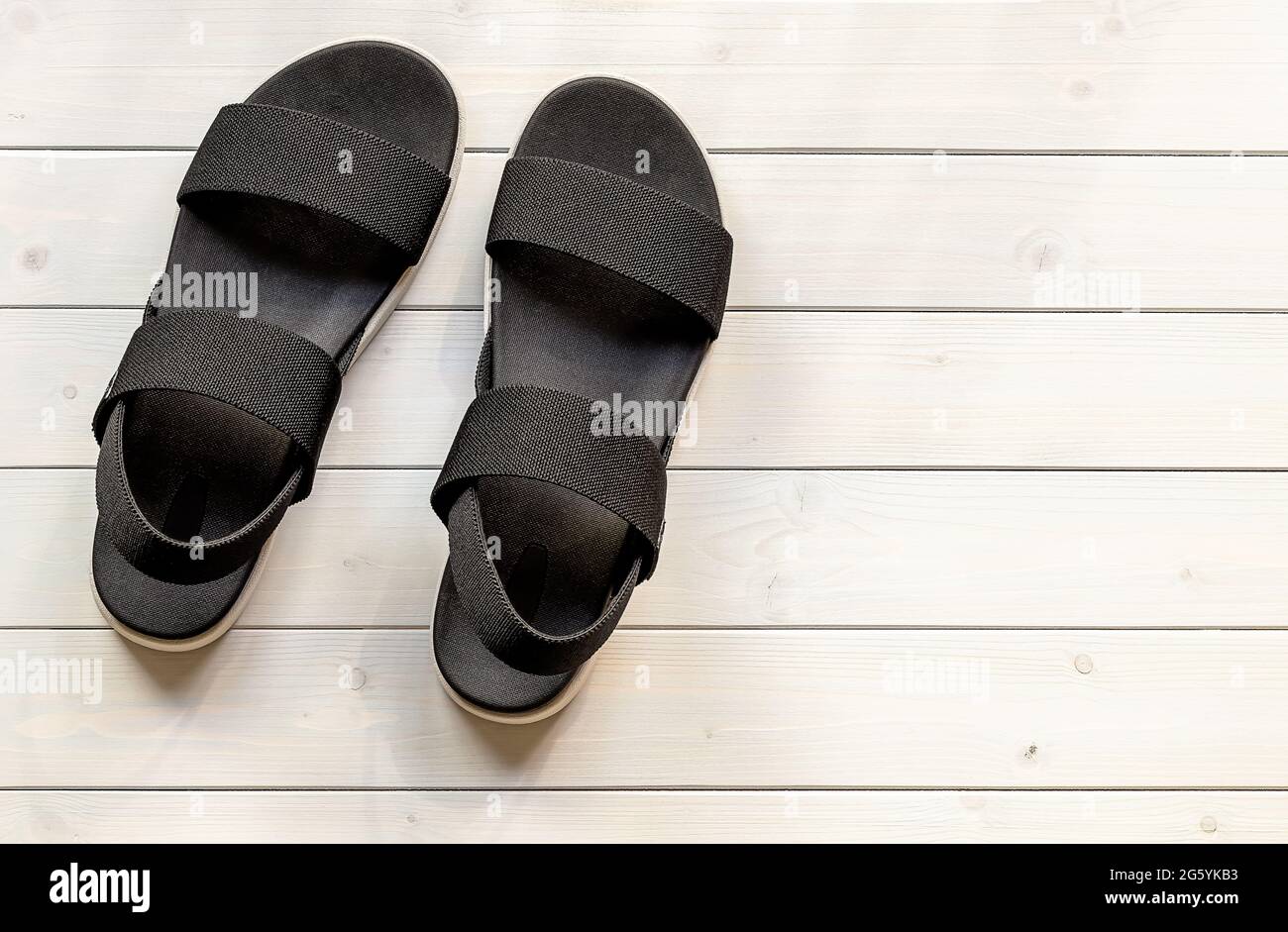 Lässige schwarze Sandalen mit offenem Zehenbereich aus recycelten Öko-Kunststofffasern für Damen auf dem weißen Holzhintergrund. Stockfoto