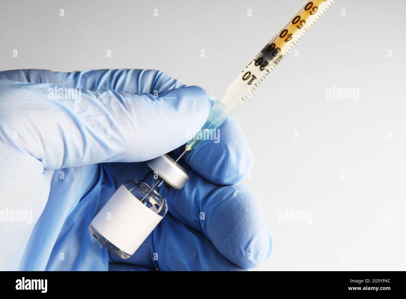 Nahaufnahme des Fläschchens mit leerem Etikett in der Hand mit Nitrilhandschuh. Flüssigkeit wird zur Injektion an die Spritze übertragen. Gesundheitswesen, Medizin, Pharmazie und vac Stockfoto