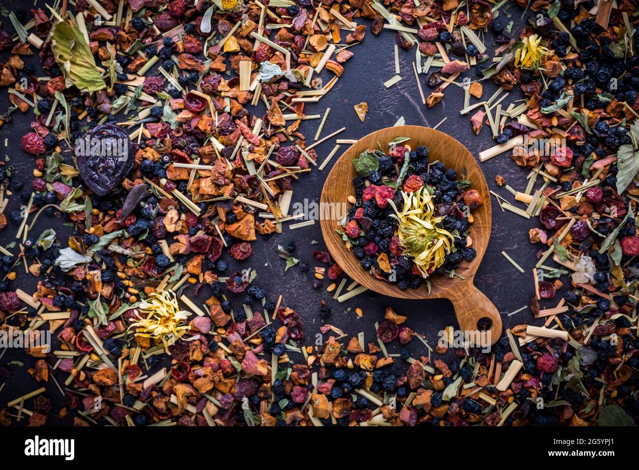 Getrocknete Teeblätter, Früchte und Beeren in Schale auf rustikalem Holztisch Stockfoto