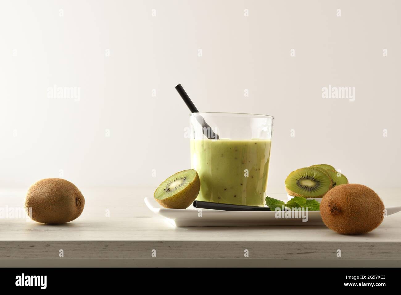 Kiwi Drink Glas Präsentation auf Teller mit geschnittenen Früchten auf Holztisch mit isoliertem Hintergrund. Vorderansicht. Stockfoto