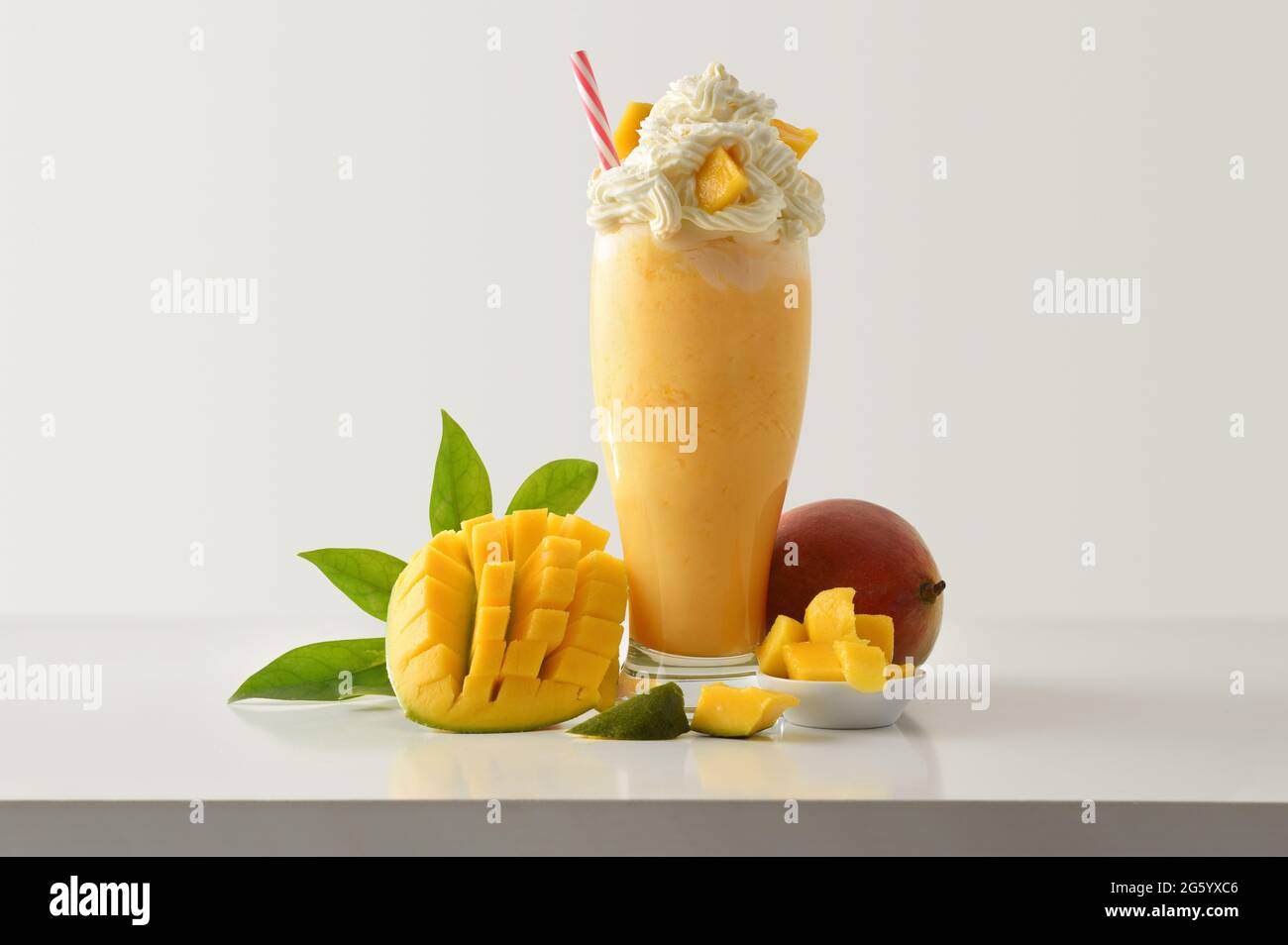 Mango-Milchshake mit cremefarbenem Dekor, mit Früchten auf weißem Holztisch und hellem, isoliertem Hintergrund. Vorderansicht. Stockfoto