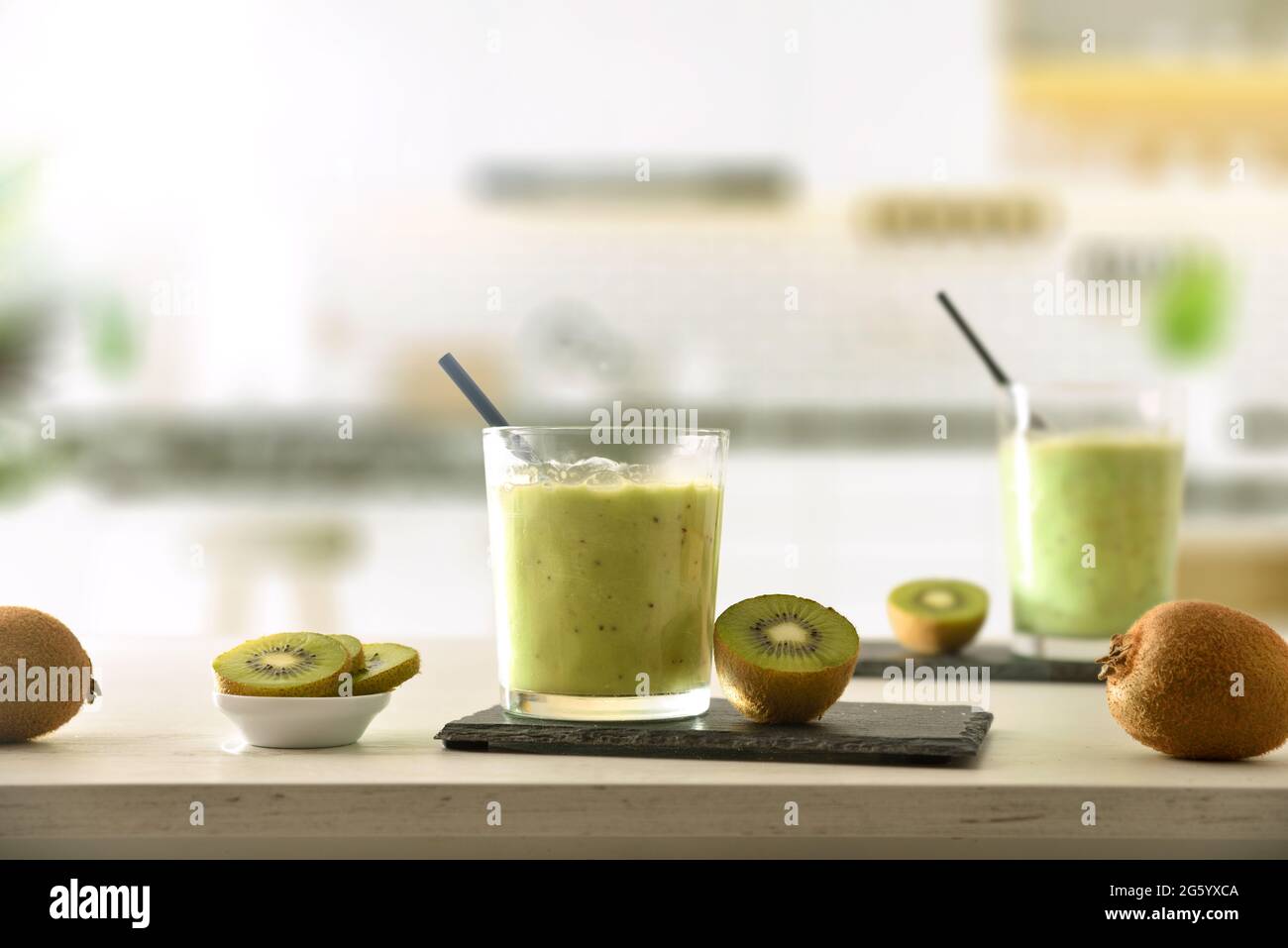 Zwei Gläser Kiwi-Getränk und Behälter mit geschnittenem Obst auf der Küchenbank. Vorderansicht. Stockfoto