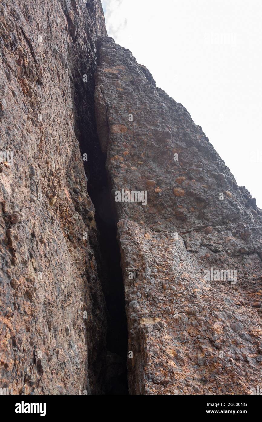 Großer Riss im Felsen, der aus kleinen runden Steinen besteht, die zusammengehalten werden. Vertikales Bild. Stockfoto