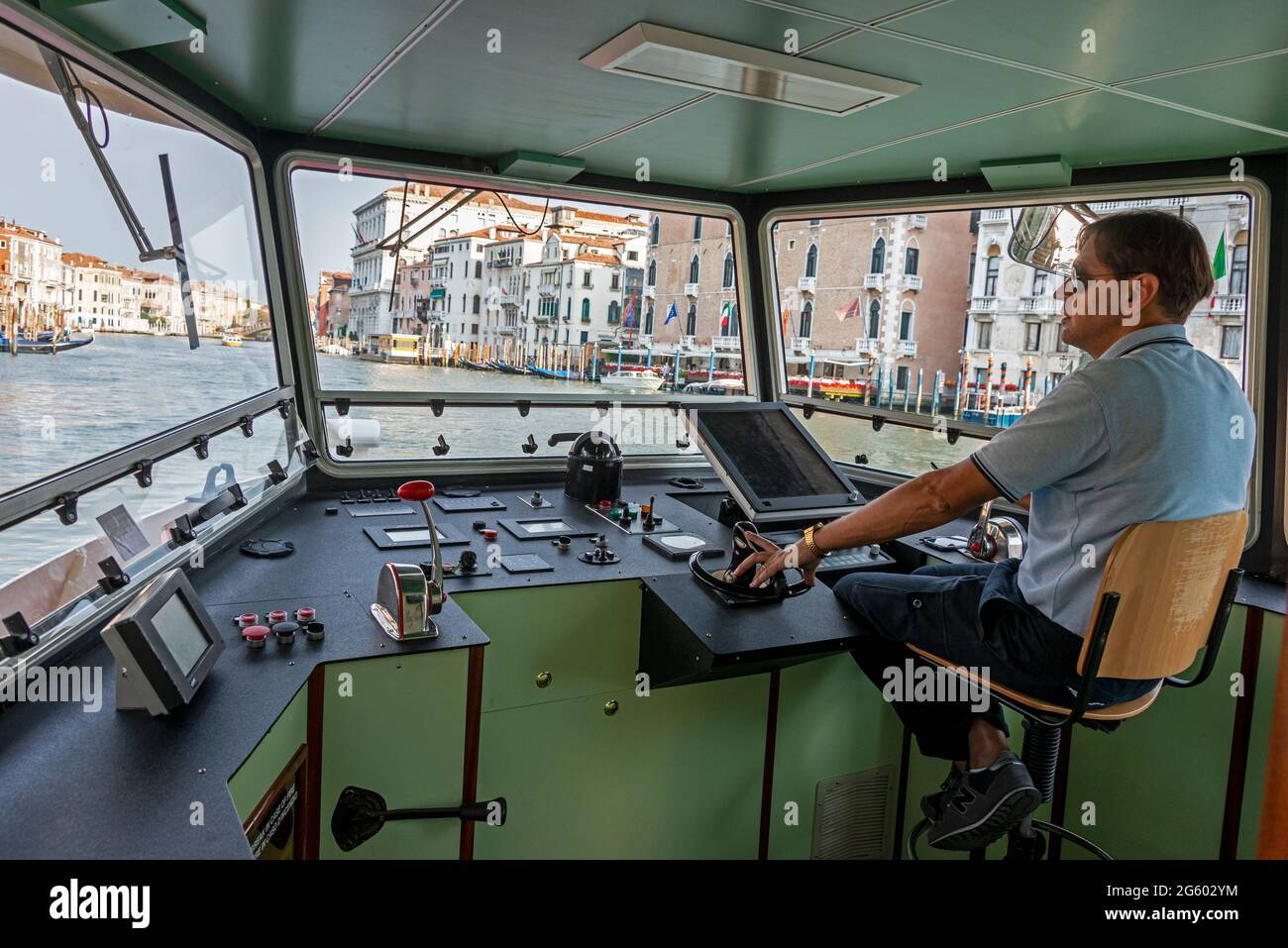 Ein Besatzungsmitglied an der Steuerung des ACTV Vaporetto – ein einstufiges Flachschiff, das einen Pendlerservice auf dem Canal Grande (Grand Canal) bietet Stockfoto