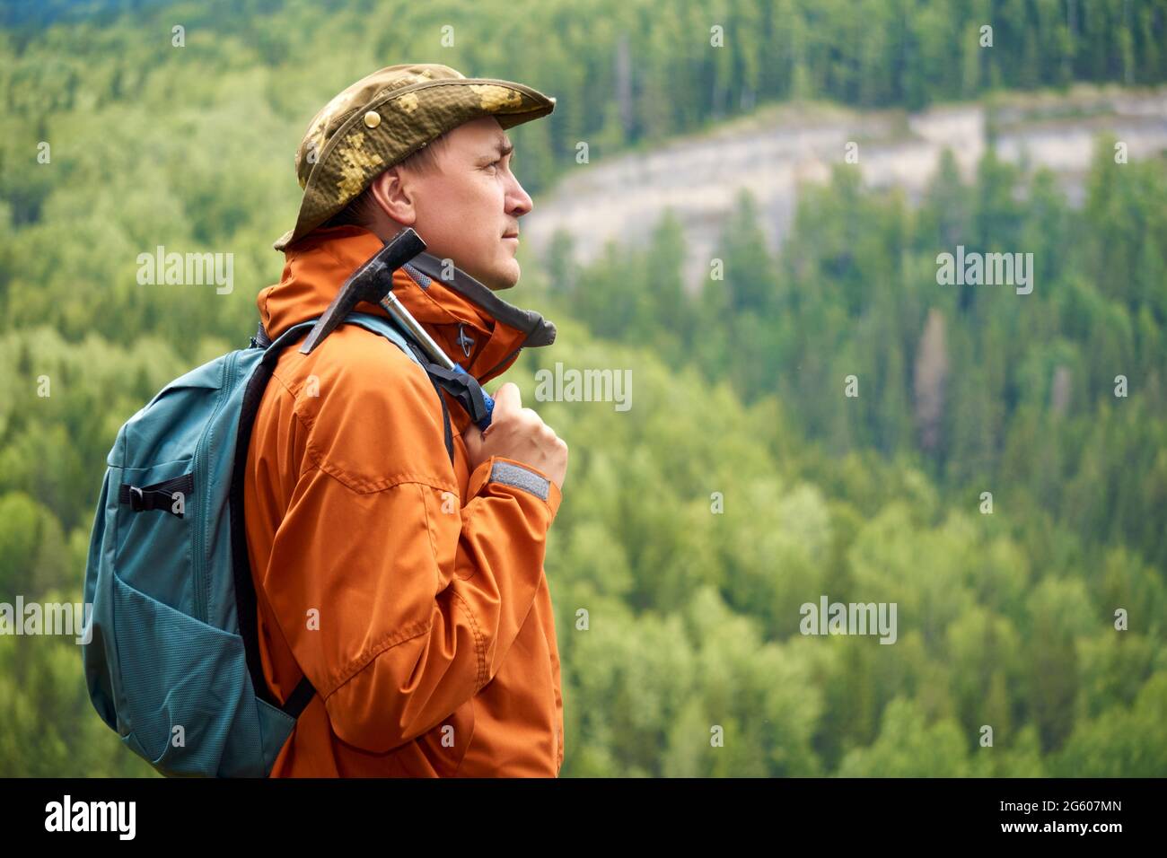 Geologe mit Rucksack und geologischem Hammer in der Hand gegen die bewaldete Berglandschaft Stockfoto