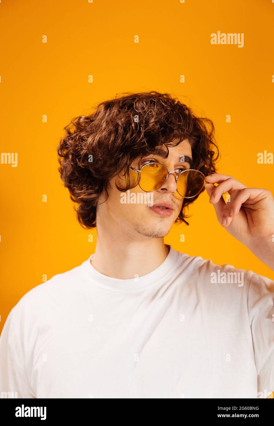 Junger lockiger Mann in weißem T-Shirt mit Sonnenbrille isoliert auf Orange Stockfoto