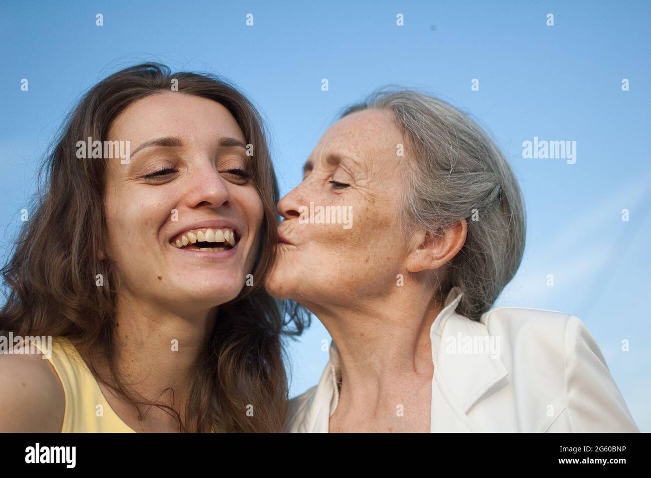 Ältere Mutter mit grauen Haaren und ihrer erwachsenen Tochter, die im Garten auf die Kamera schaut und sich an sonnigen Tagen im Freien umarmt, Muttertag Stockfoto