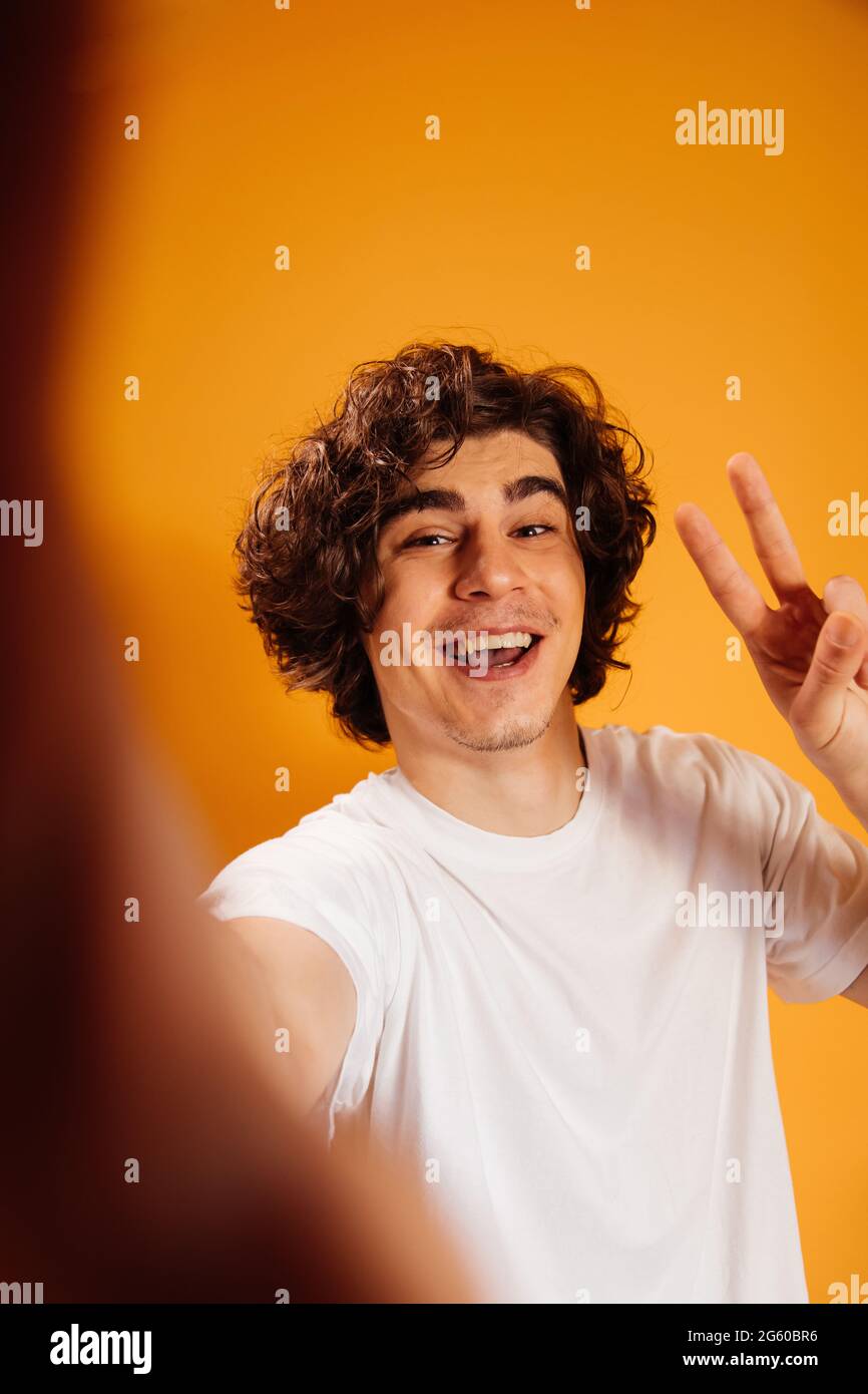 Fröhlicher Mann im weißen T-Shirt mit Friedenszeichen auf orangefarbenem Hintergrund Stockfoto