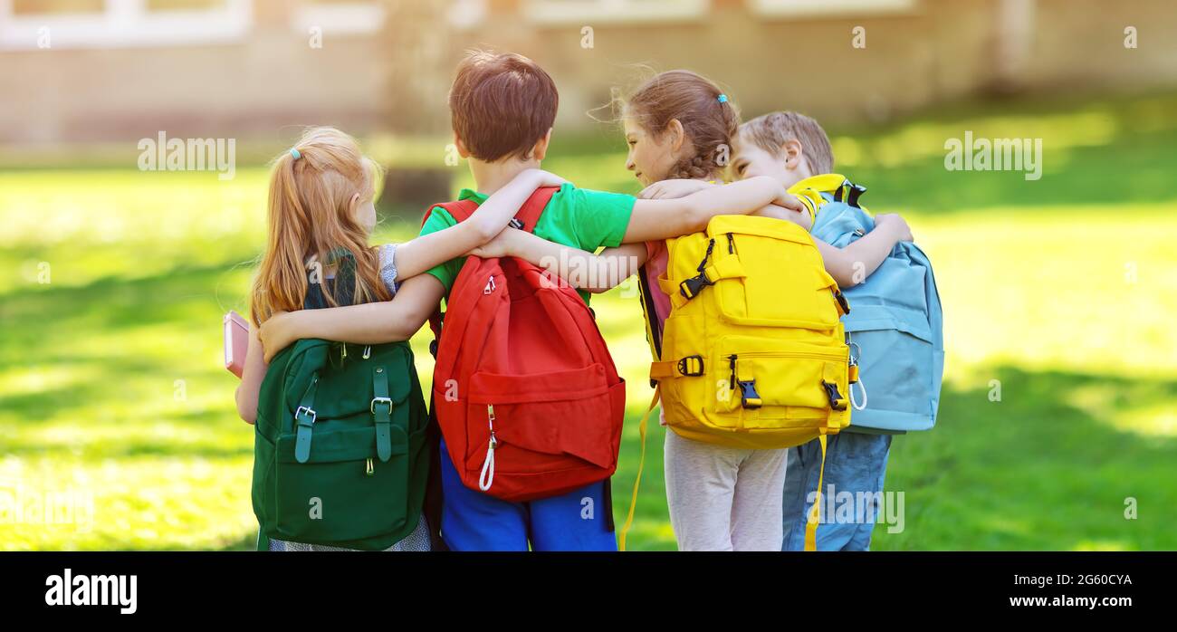 Eine Gruppe von Kindern mit Rucksäcken steht im Park in der Nähe der Schule Stockfoto