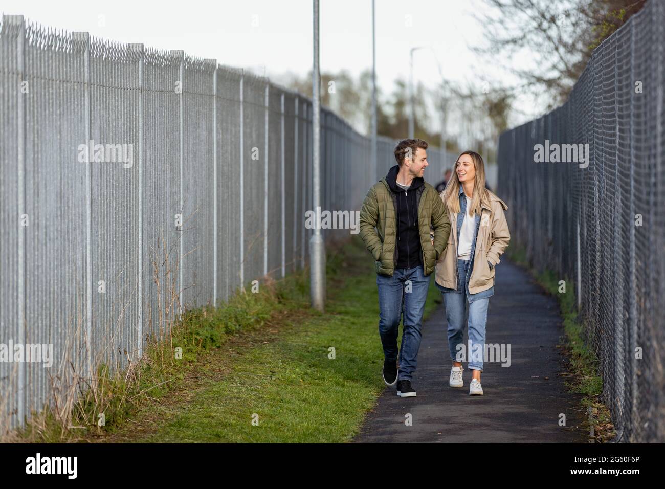 Eine Frontansicht eines kaukasischen Paares mittlerer Erwachsenen, das zusammen einen Fußweg entlang läuft, lächelt und die Gesellschaft der anderen genießt. Stockfoto