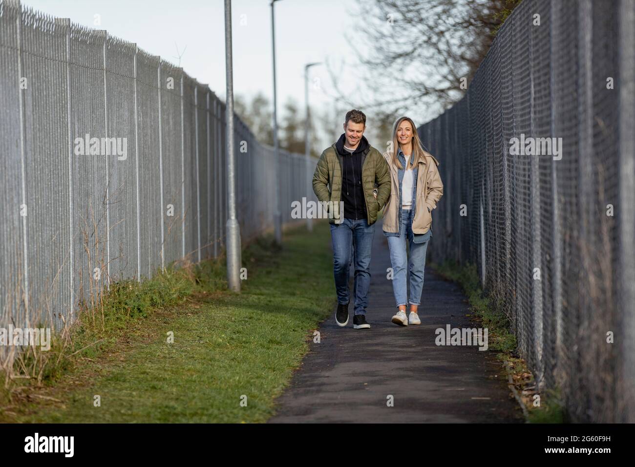 Eine Frontansicht eines kaukasischen Paares mittlerer Erwachsenen, das zusammen einen Fußweg entlang läuft, lächelt und die Gesellschaft der anderen genießt. Stockfoto