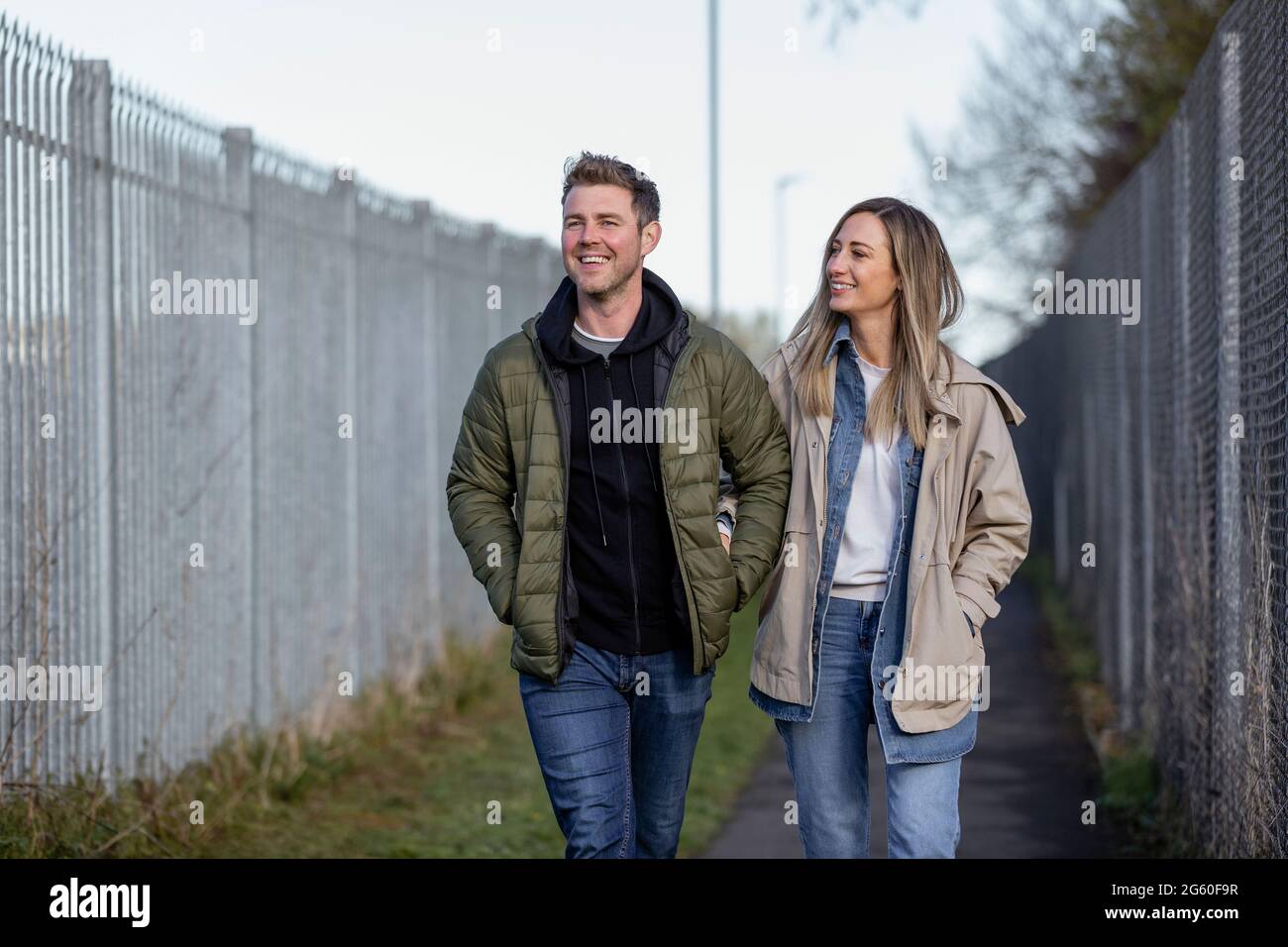 Eine Frontansicht eines kaukasischen Paares mittlerer Erwachsenen, das zusammen einen Fußweg entlang läuft, lächelt und die Gesellschaft der anderen genießt. Stockfoto