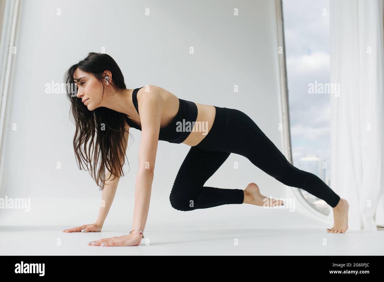 Barfuß armenische Frau praktiziert Yoga in einbeiniger Plankenpose auf weißem Boden Stockfoto