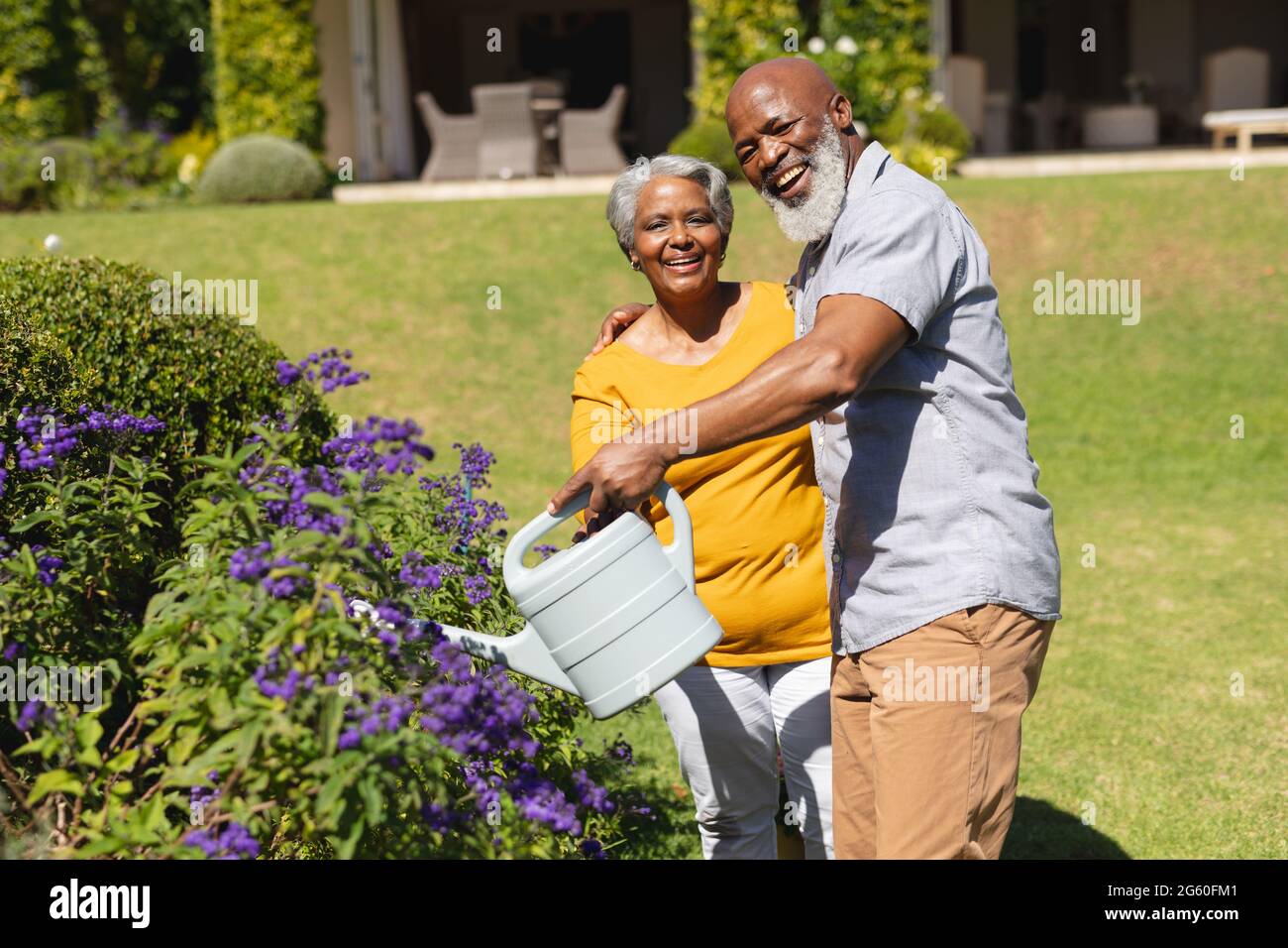 Porträt eines älteren afroamerikanischen Paares, das Zeit im sonnigen Garten verbringt und Blumen gießt Stockfoto