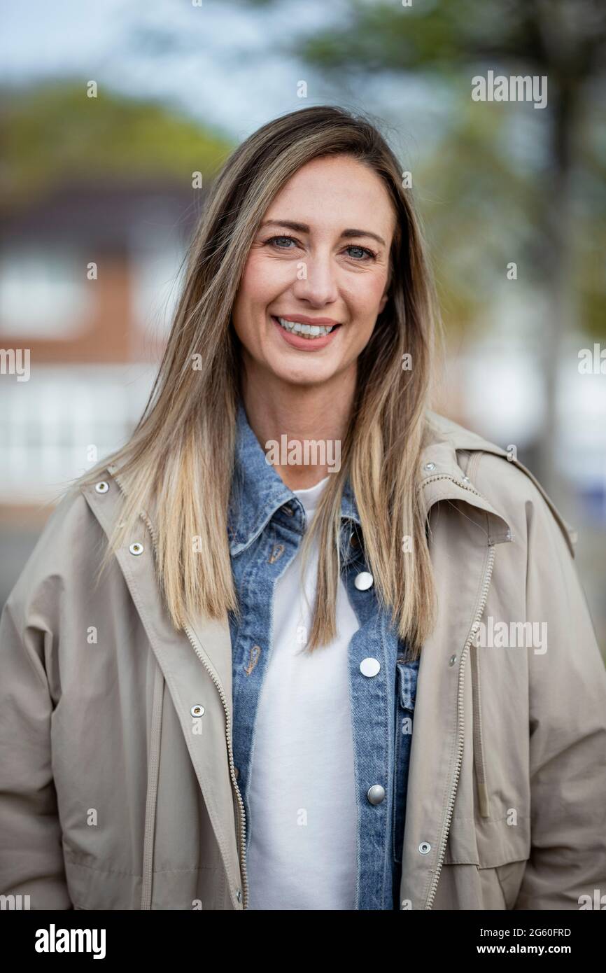 Eine Frontansicht-Portraitaufnahme einer kaukasischen Frau mittleren Erwachsenen in legerer Kleidung, sie lächelt und schaut auf die Kamera. Stockfoto
