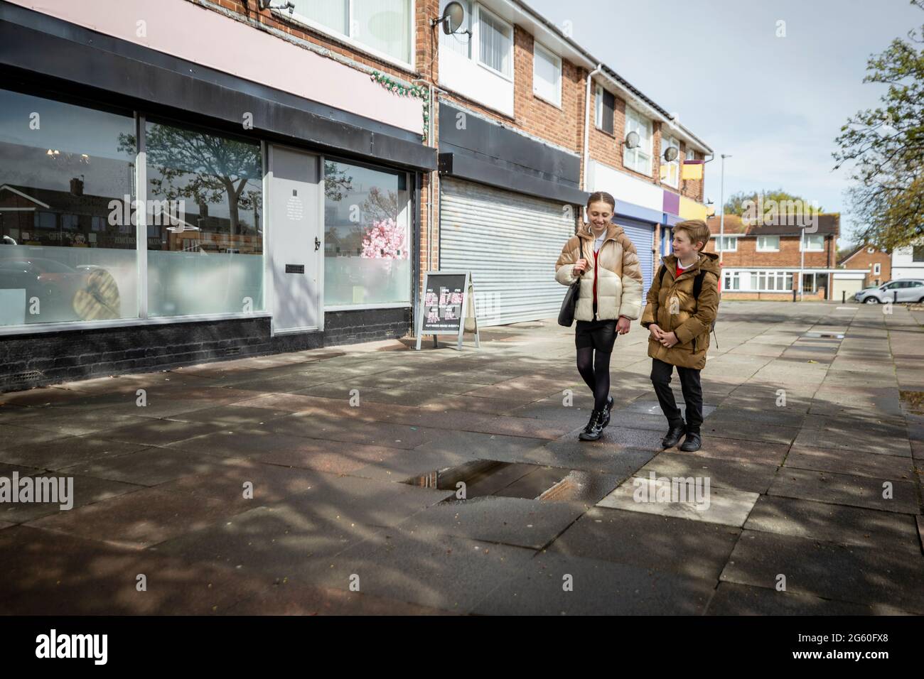 Eine Aufnahme eines jungen Bruders und einer Schwester, die einen Straßenweg entlang gehen und von der Schule nach Hause gehen. Stockfoto